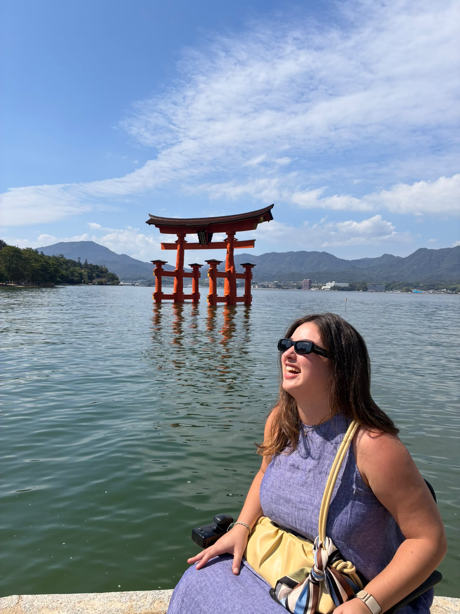 宮島の海辺で、厳島神社の大鳥居を背景に笑顔を見せる車いすを利用するお客様。
